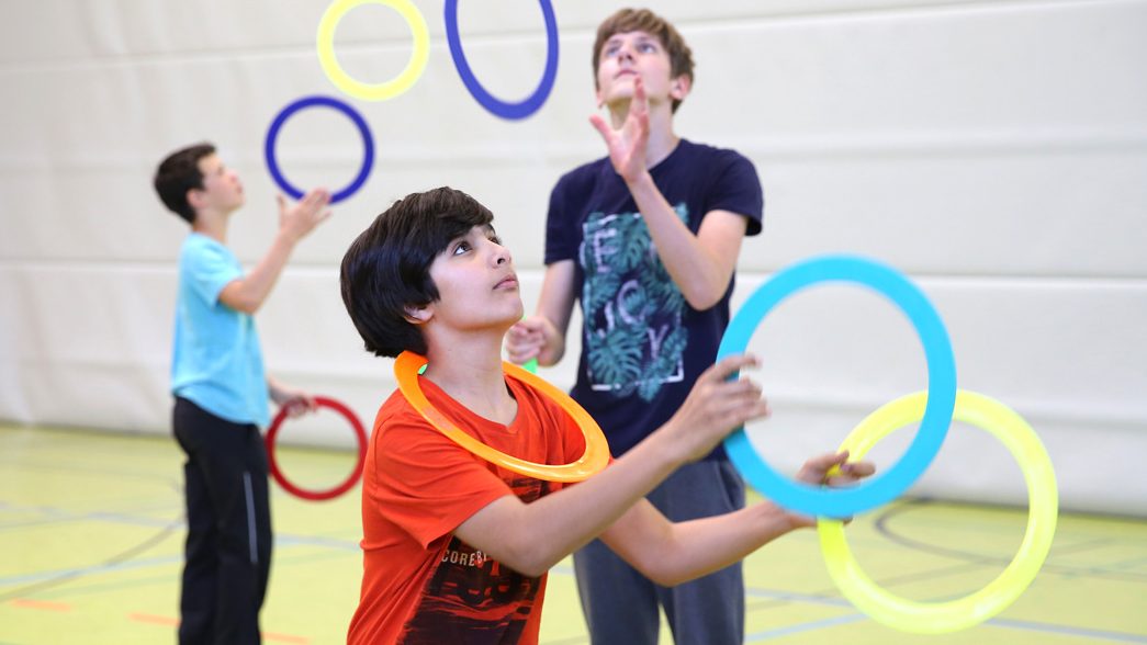 Schüler jonglieren mit bunten Ringen in der Sporthalle.
