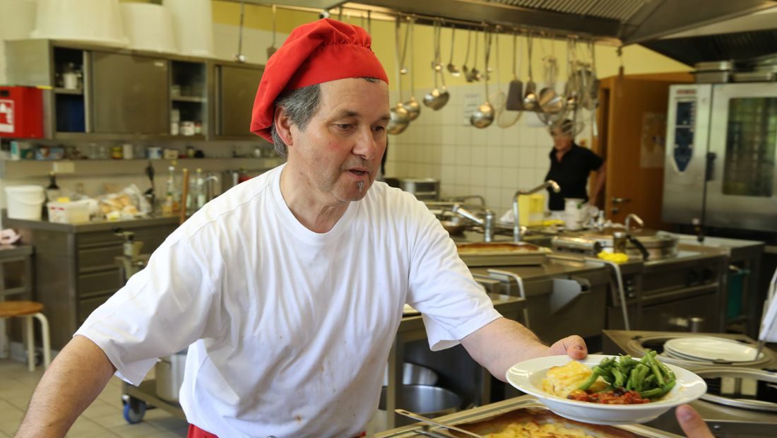 Koch der Schulküche reicht ein angerichtetes Mittagessen aus.