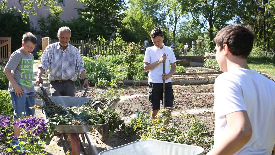 Schüler arbeiten mit dem Lehrer im Schulgarten.