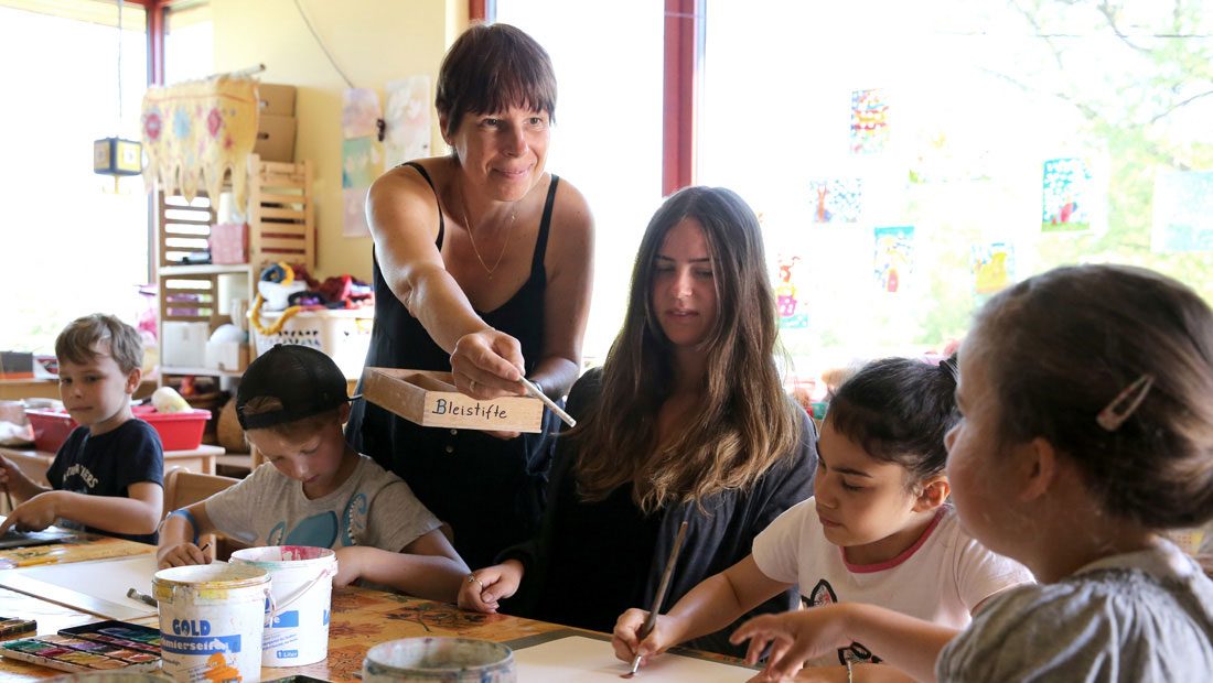 Betreuerin unterstützt Kinder beim Malen im Hort.