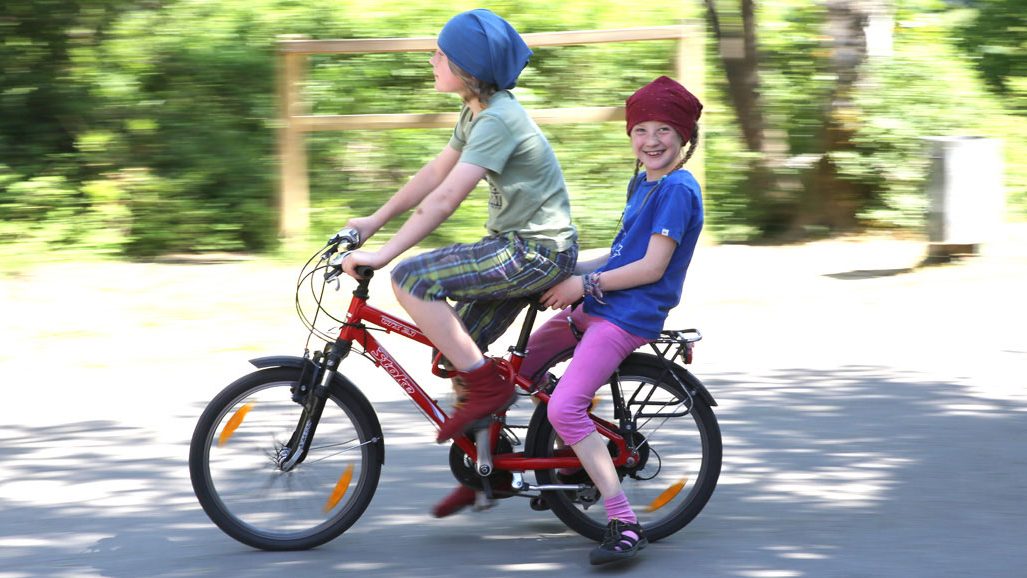 Zwei Kinder fahren gemeinsam Fahrrad auf dem Schulgelände.