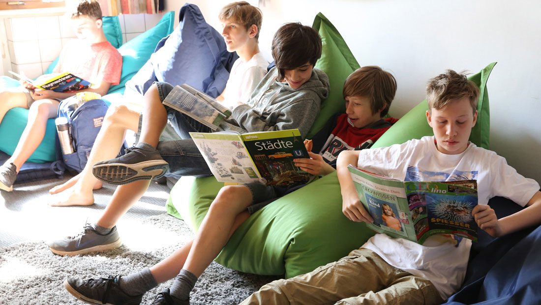 Schüler lesen in der Schülerbibliothek auf Sitzkissen.